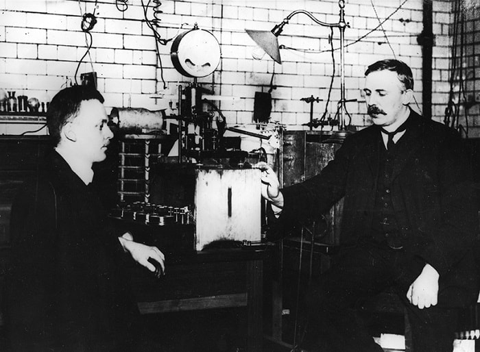 Ernest Rutherford ve Hans Geiger'in alfa parçacıklarını sayan aparat ile birlikte resmedildiği 1912 tarihli fotoğraf