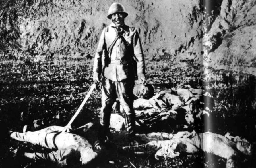 Sırıtan bir Japon askeri, elinde bir kurbanın kesik başını tutuyor.
