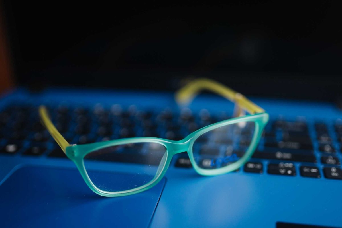 Mavi bir dizüstü bilgisayar üzerinde açık mavi çerçeveli gözlüklerin yakın çekimi.