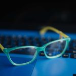 Mavi bir dizüstü bilgisayar üzerinde açık mavi çerçeveli gözlüklerin yakın çekimi.